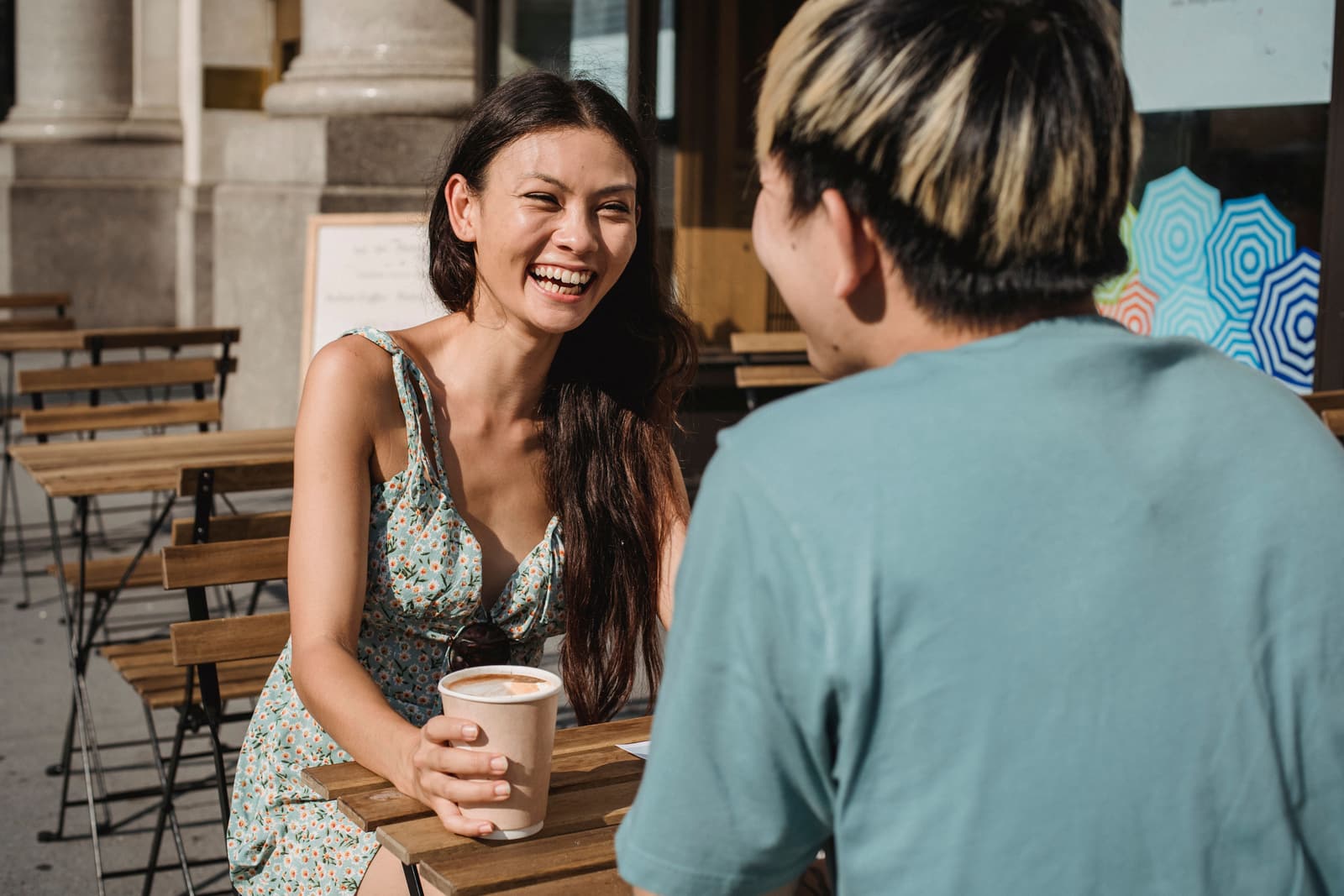 Friends laughing together over coffee at a sunny street table