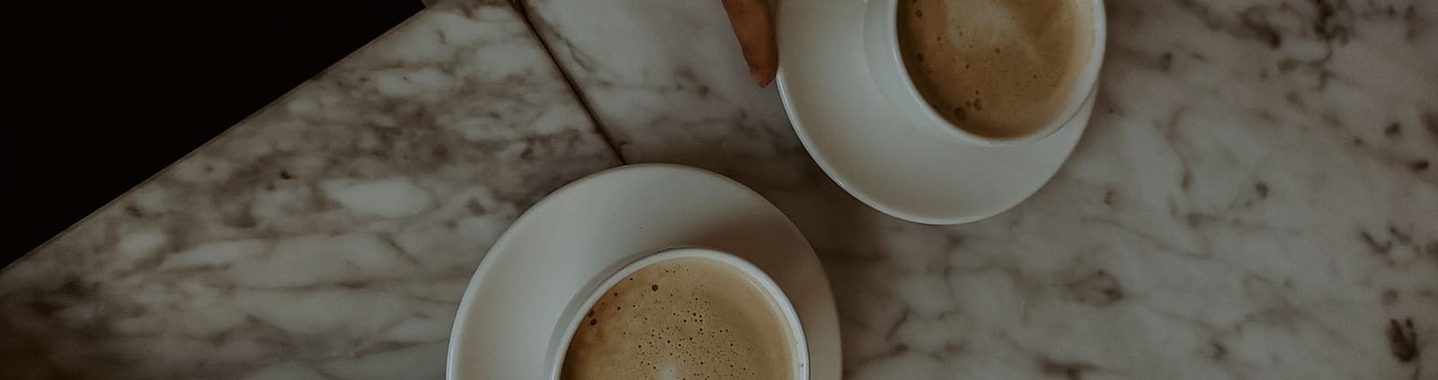 Two coffee cups on a marble table, reaching toward each other